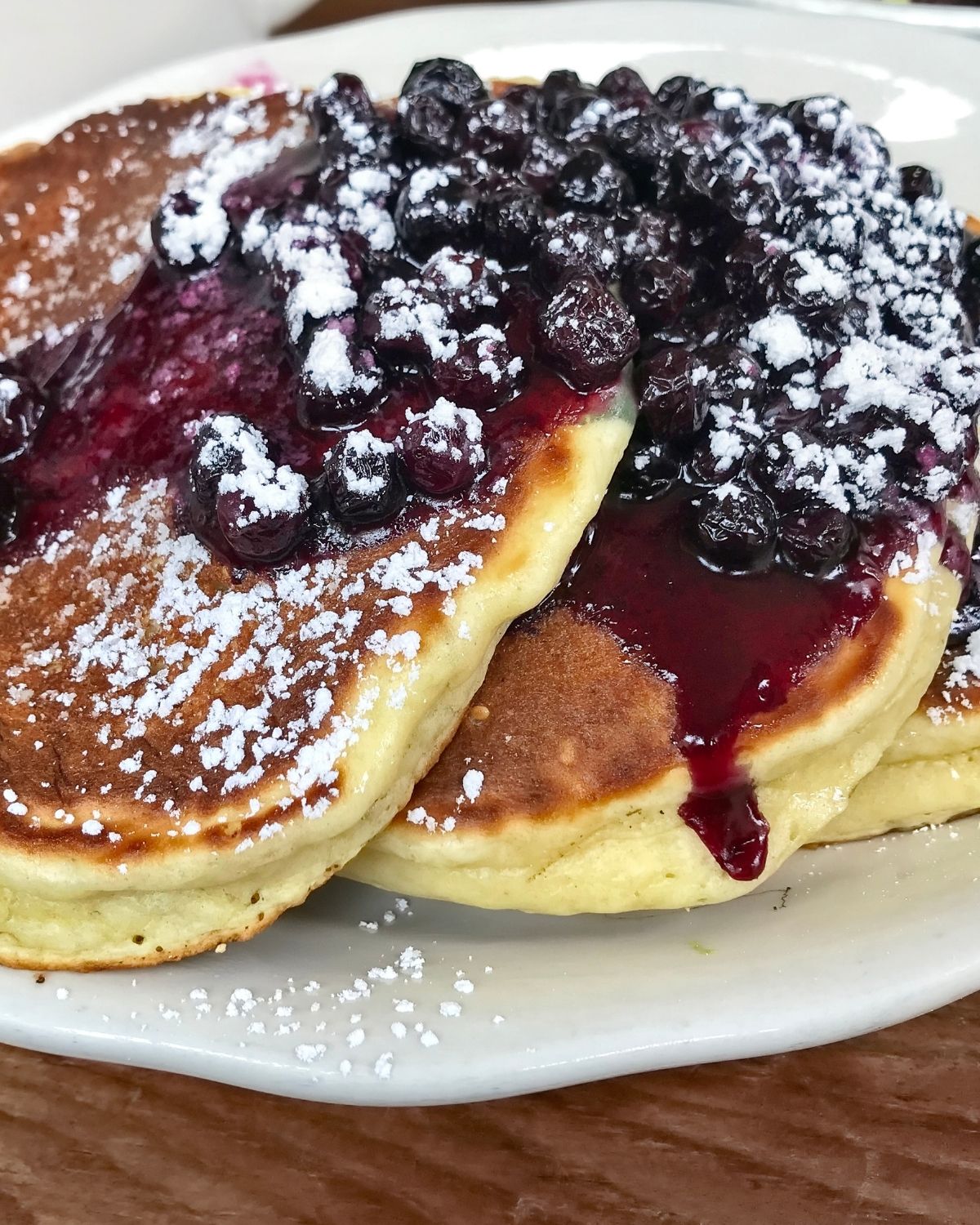 Lemon Pancakes with Blueberry Compote on a white dish with powdered sugar.