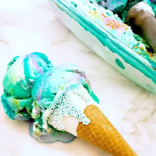 A cone of two scoops of teal ice cream lying on a table