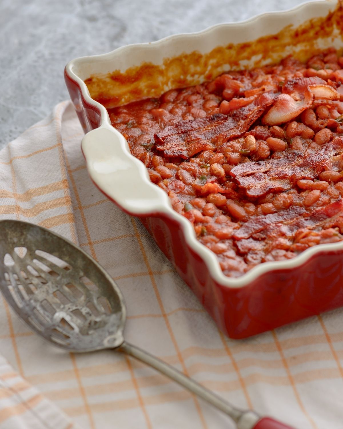 A serving spoon and a cassorle dish of baked beans.