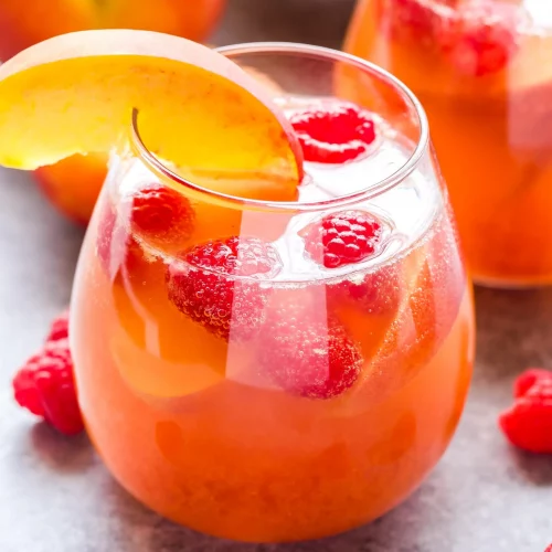 A glass of Peach Rosé Sangria garnished with raspberries and peach slices