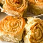 Golden brown Pull Apart Pizza Bread buns topped with sesame seeds are arranged on a white plate, with a few pieces placed in the foreground on a white surface.