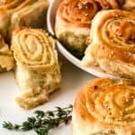 Golden brown, spiral-shaped Pull Apart Pizza Bread rolls with sesame seeds on top, arranged on a white plate and surface, garnished with fresh thyme.