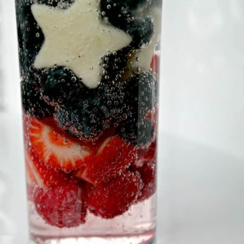 A glass filled with sprite, strawberries, blueberries and apples cut into stars
