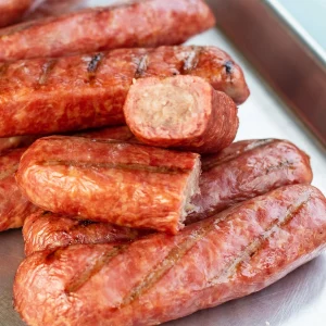 Many smoked bratwursts on a plate, one is sliced to reveal a cross section