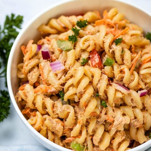 Spicy tuna pasta salad with an orange hue with onion, tomato and herbs