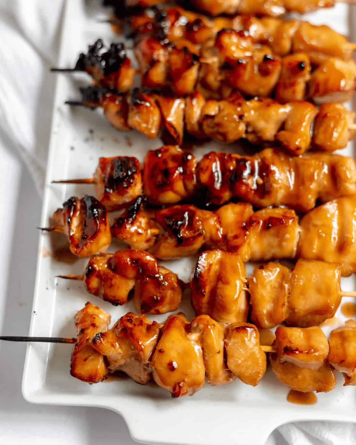 Grilled skewers coated in a glossy sauce, arranged on a white rectangular plate.