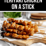 Grilled teriyaki chicken skewers on a wooden board, with a blurred background featuring greenery and elegant wooden dishes, perfectly showcasing teriyaki chicken on a stick.