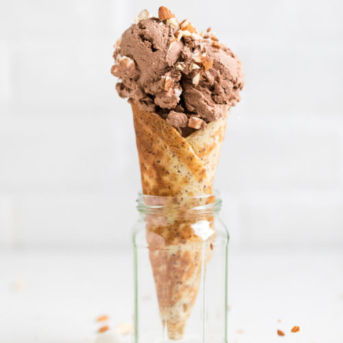 A small glass jar holds a waffle cone that holds a scoop of rocky road ice cream