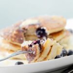 A fork with blueberry pancakes on a plate.
