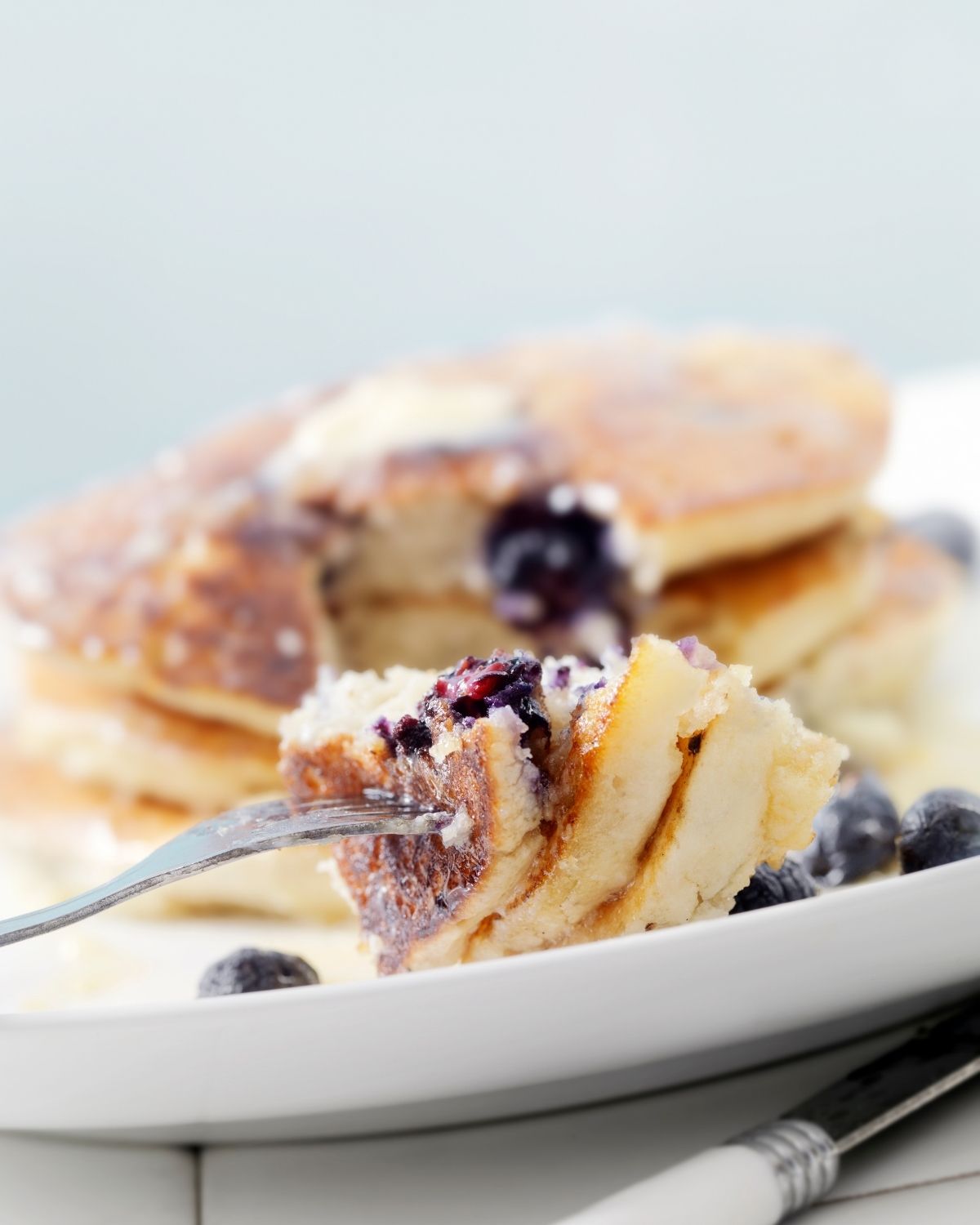 A fork with blueberry pancakes on a plate.