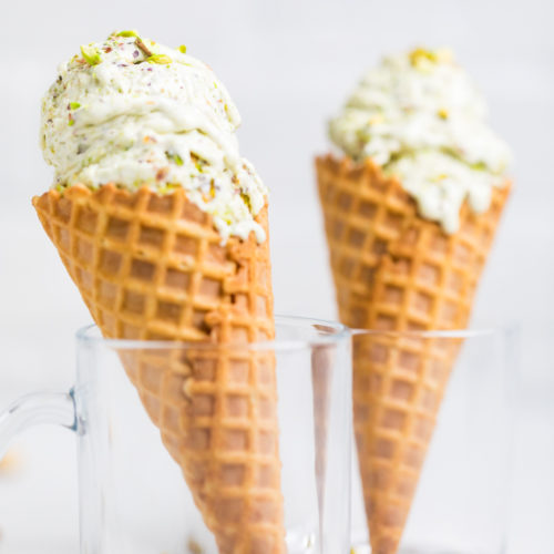 Two waffle cones both with a scoop of pistachio ice cream