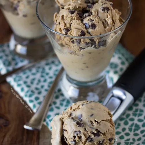 A glass filled with espresso chocolate chip ice cream. An ice cream scooper with a scoop of said ice cream sits in front of it.
