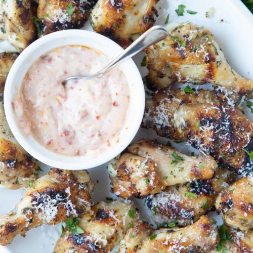 A plate of garlic herb baked wings surround a bowl of pinkish sauce