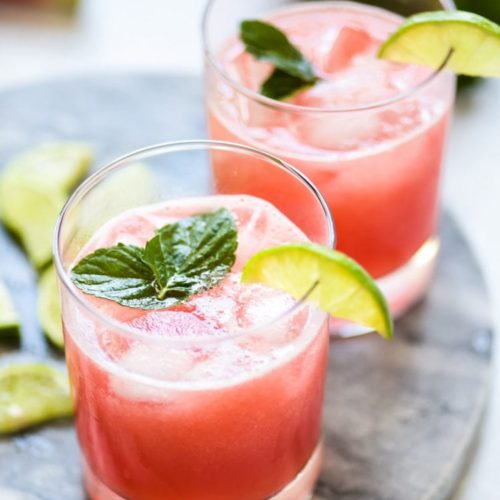 Two glasses of Watermelon Aqua Fresca garnished of a lime and mint leaf