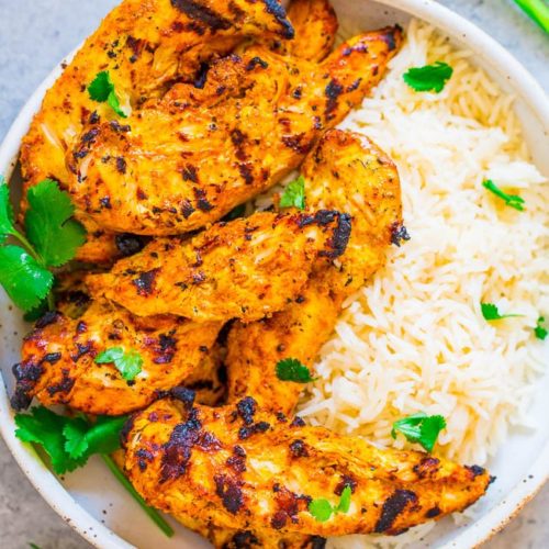 A plate of grilled tandoori chicken with herbs next to a side of white rice