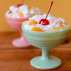 Two small dishes are filled with ambrosia salad covered in cool whip with a cherry on top