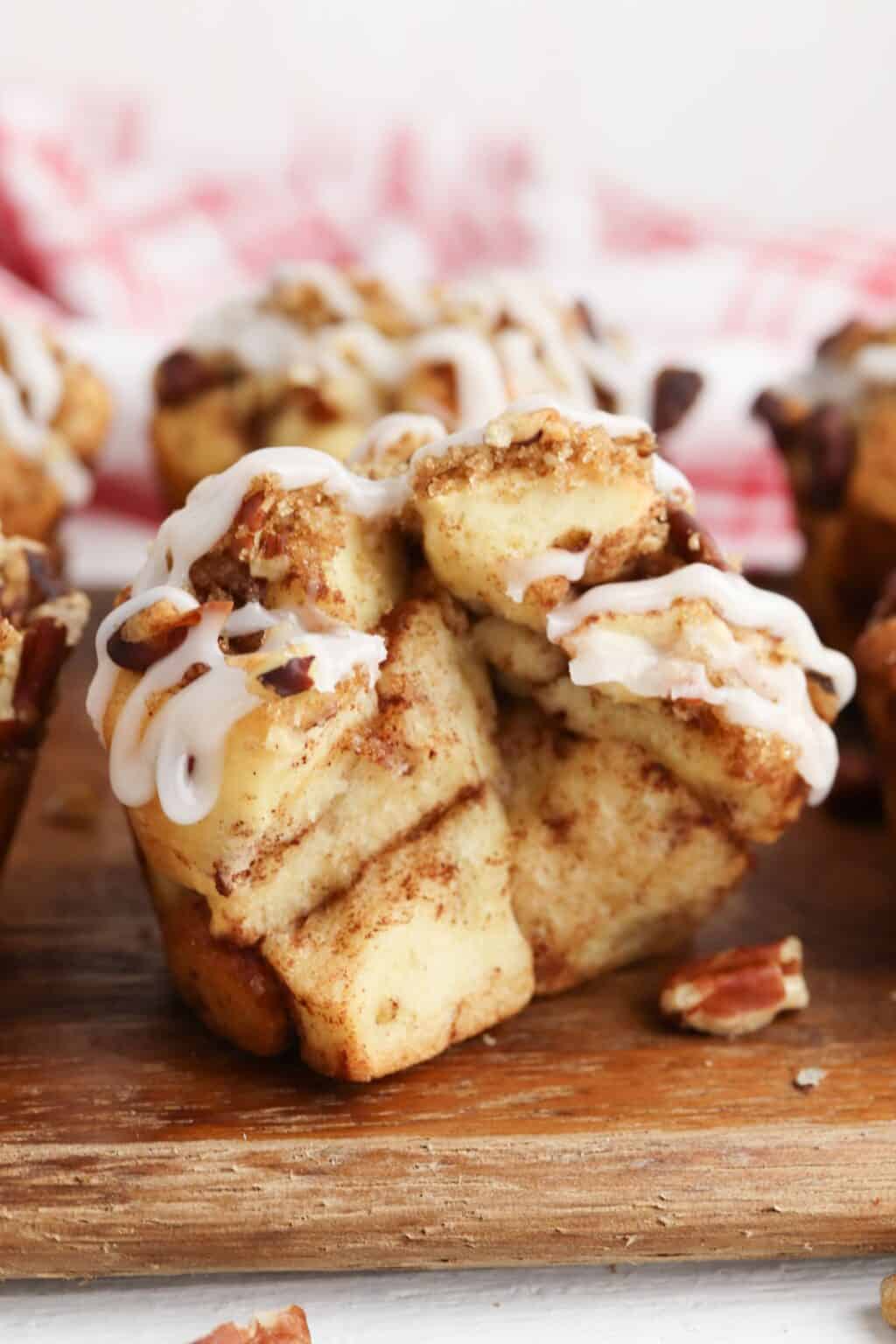 A close-up of Cinnamon Roll Muffins topped with white icing and small pieces of pecans, placed on a wooden surface.