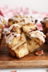 A close-up of Cinnamon Roll Muffins topped with white icing and small pieces of pecans, placed on a wooden surface.