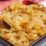 A close-up of Crockpot Caramelized Onions in a small square bowl, with a red cloth in the background.