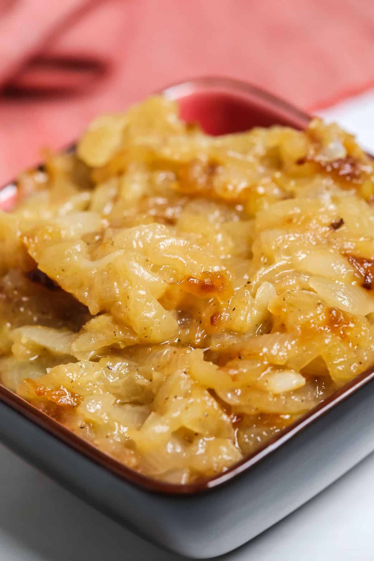 A close-up of Crockpot Caramelized Onions in a small square bowl, with a red cloth in the background.