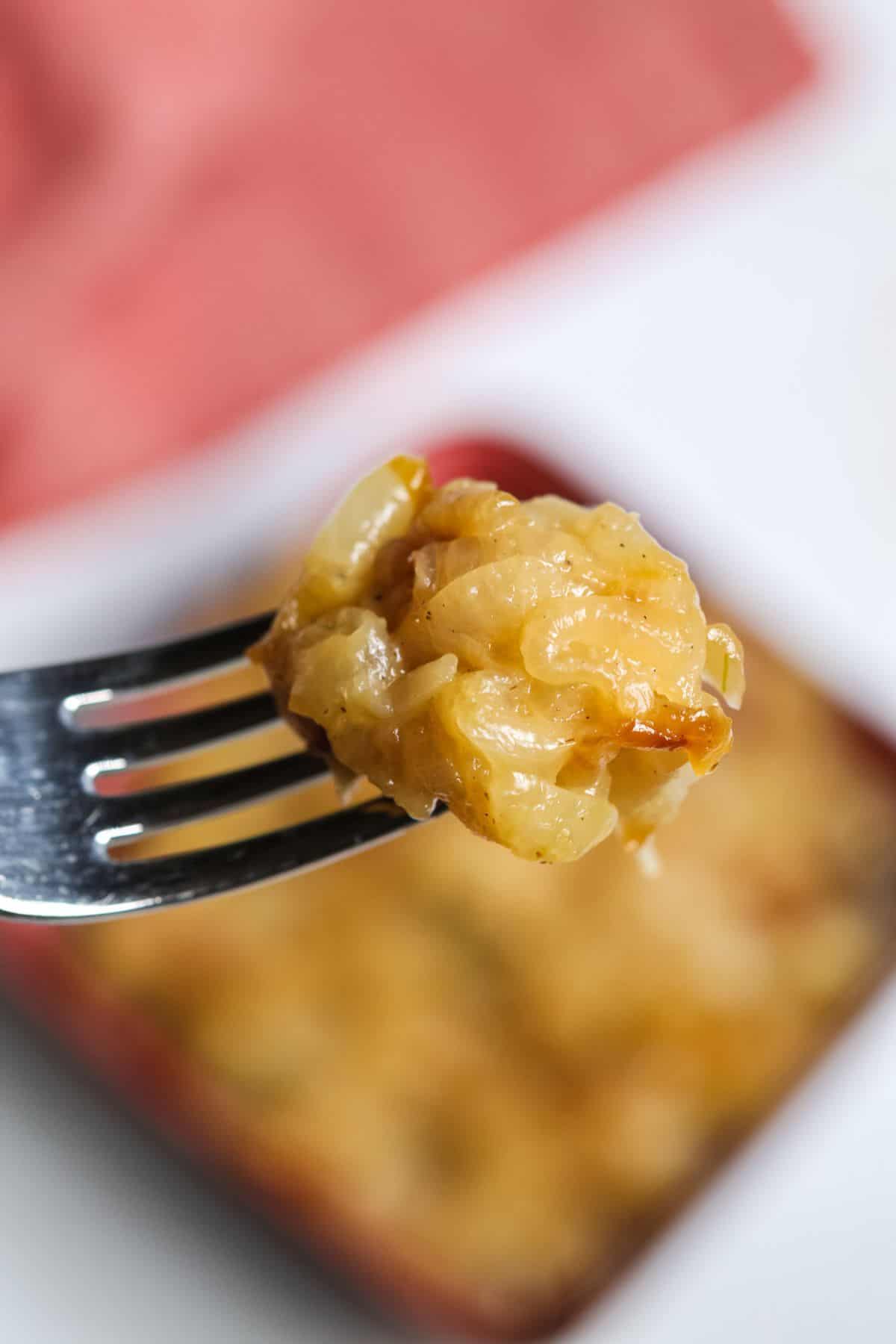 A fork holds a bite In the background, a baking dish of the same dish appears blurred.