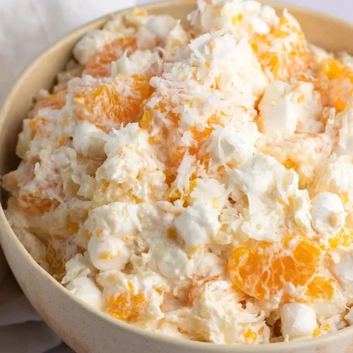 A bowl filled with ambrosia salad with oranges, pineapples, and marshmallows
