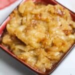 A small red bowl filled with Crockpot Caramelized Onions sits on a white surface.