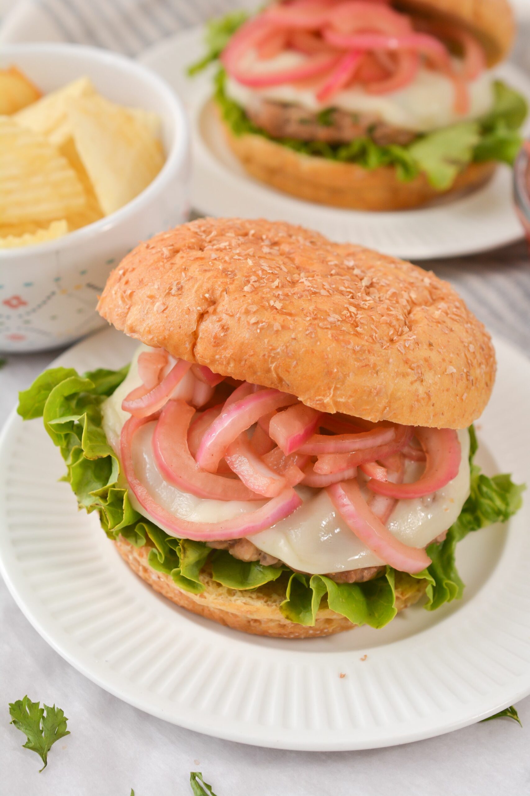 Grilled Turkey Burgers with Pickled Onions on a white plate with chips in the background.