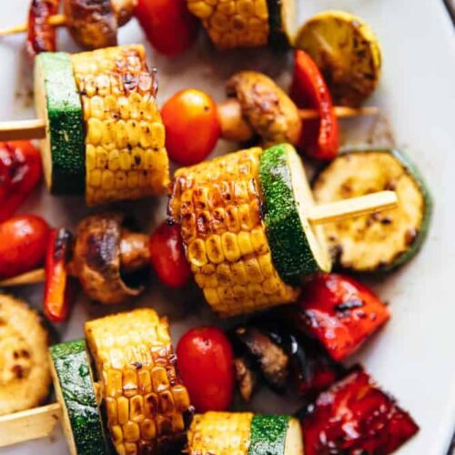 A plate of grilled vegetable kabobs, including corn, zucchini, peppers, and mushrooms