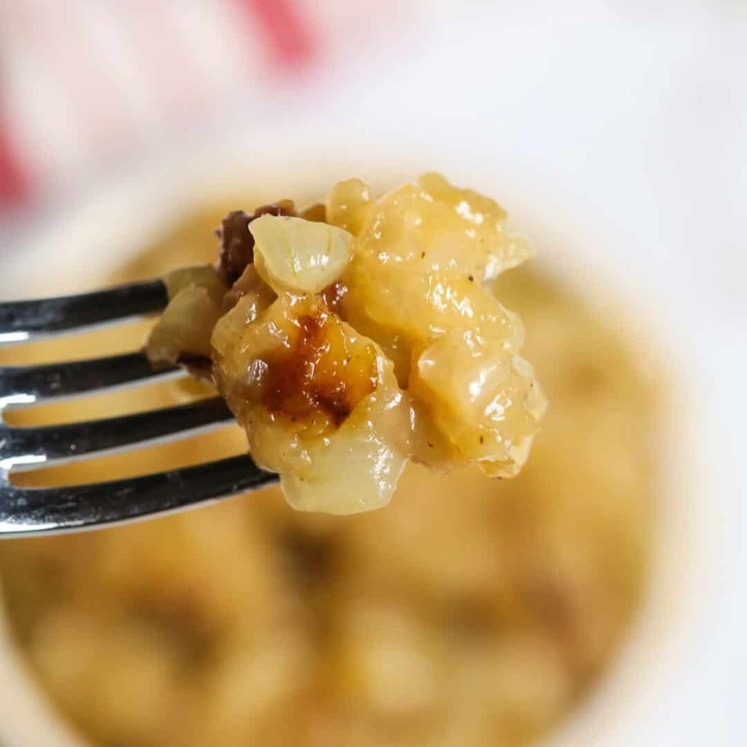 A close-up of a fork holding a bite of cheesy, baked onion casserole with visible Instant Pot Caramelized Onions.