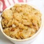 A white bowl filled with Instant Pot Caramelized Onions sits on a white surface, with a red and white striped cloth in the background.