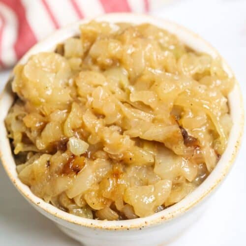 A white bowl filled with Instant Pot Caramelized Onions sits on a white surface, with a red and white striped cloth in the background.