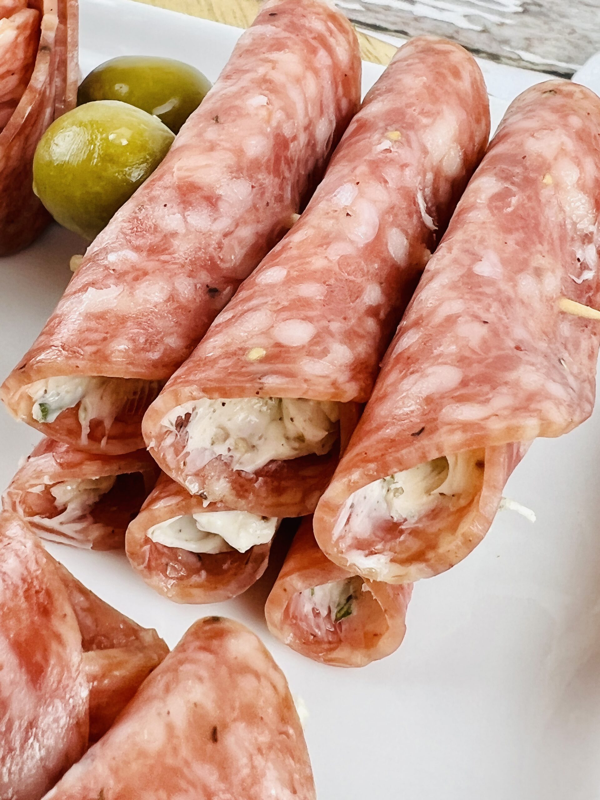 Salami Cream Cheese Roll Ups with green olives on a white plate.
