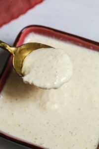 A spoon holding a thick, creamy white Tiger Sauce hovers over a bowl filled with the same tangy, flavorful sauce.