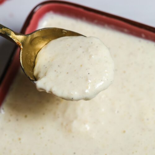 A spoon holding a thick, creamy white Tiger Sauce hovers over a bowl filled with the same tangy, flavorful sauce.
