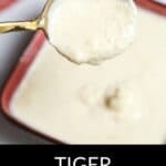 A spoon holds a creamy, white Tiger Sauce above a bowl filled with the same savory sauce. Text at the bottom reads "TIGER SAUCE.