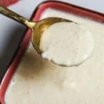 A close-up of a spoon holding creamy white Tiger Sauce above a red bowl filled with the same zesty sauce.