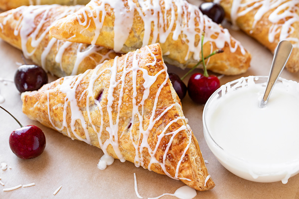 Cherry turnovers with a cup of sweet glaze on the side