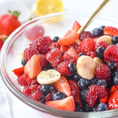 A large bowl is filled with a variety of berries and bananas, topped with a lemon honey dressing