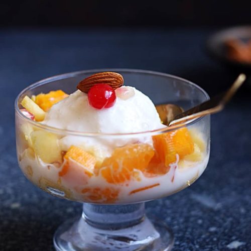 A small dish is filled with oranges and pineapple with a scoop of vanilla ice cream and a cherry on top
