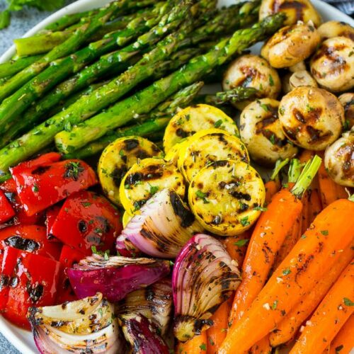 A large plate of grilled vegetables containing asparagus, mushrooms, carrots, onions, peppers, and squash