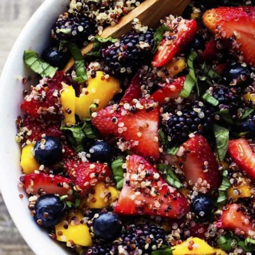 An overhead shot of a fresh fruit salad sprinkled with quinoa seeds and honey lime dressing