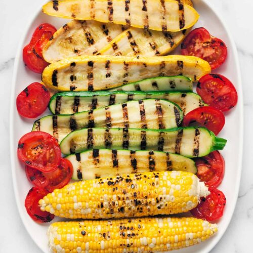 An overhead shot of grilled squash, zucchini, corn, and tomatoes