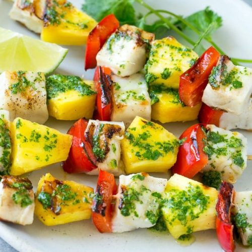 A plate with several kabobs with fish, peppers and pineapple garnished with parsley