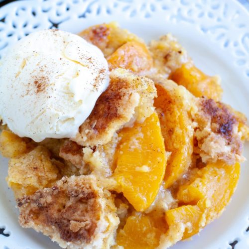 Peach cobbler on a plate with a scoop of vanilla ice cream over it
