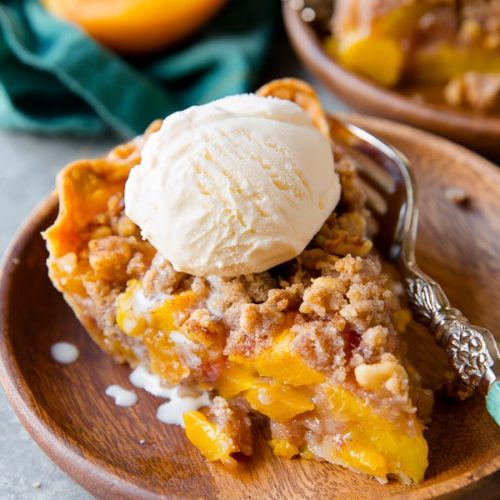 peach crumble pie on plate with ice cream scoop on top
