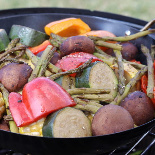 A cast iron pan in filled with various vegetables over a smoker