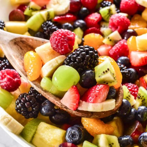 A clseup of a fruit salad with many fresh fruits like grapes, blackberries, strawberries, bananas, and others