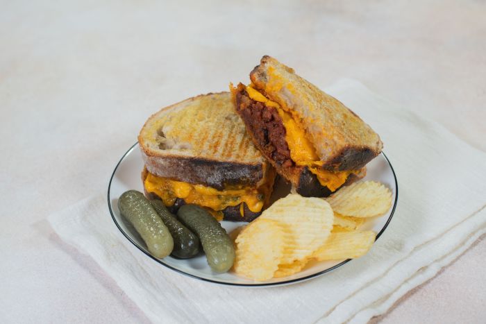 A Vegan Sloppy Joe Grilled Cheese with pickles and chips on the side