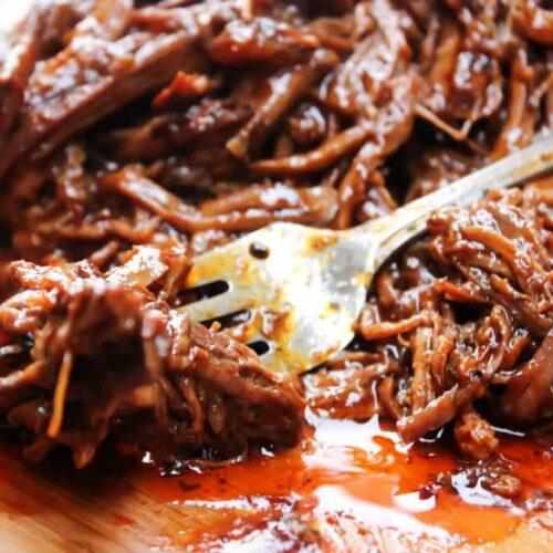 Shreds of beef brisket lay on a cutting board with a fork resting in it